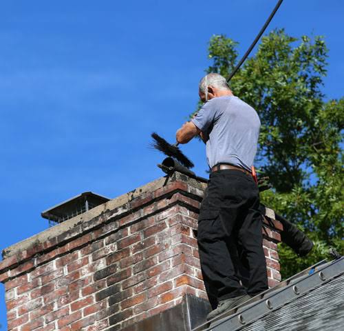 Chimney sweep working at the top of a weathered brick chimney