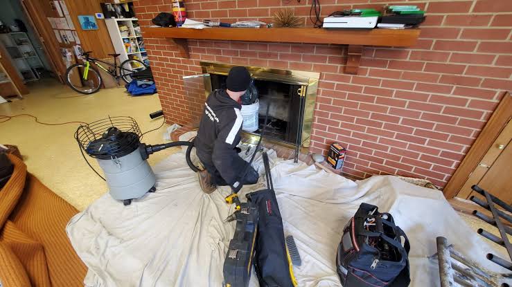 Chimney sweep cleaning a brick fireplace with protective floor coverings