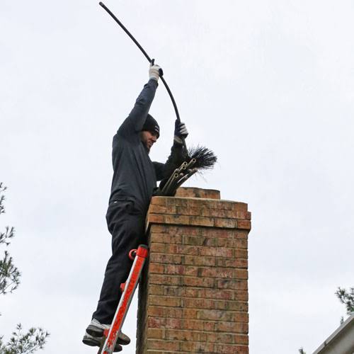 Chimney sweep raising a flexible brush above a brick chimney