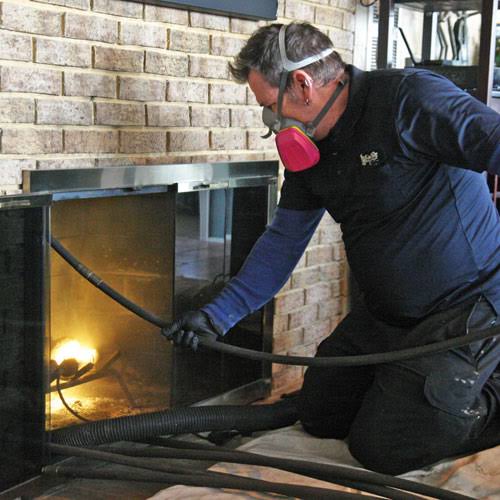 Professional cleaning a residential fireplace with protective equipment